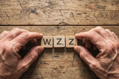 Mains arrangeant des tuiles de Scrabble en bois formant des mots de 3 lettres avec W et Z sur une table en chêne